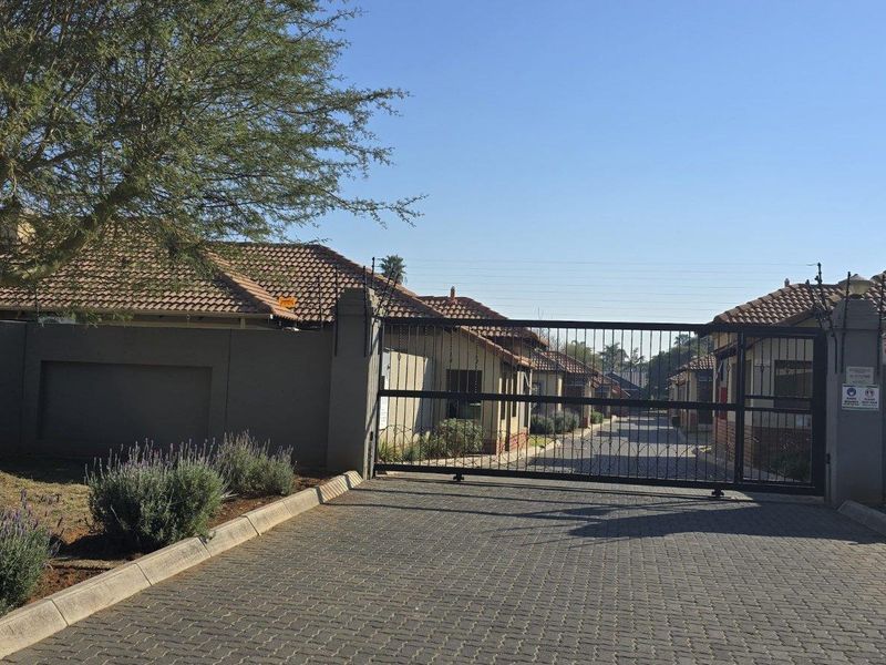 View of the secure gated entrance to the townhouse complex, featuring a paved driveway and perimeter walling.