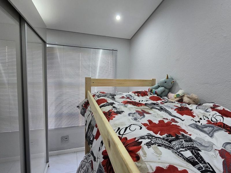 A well-maintained bedroom featuring built-in sliding door wardrobes, tiled flooring, and venetian blinds, providing a clean and functional living space.