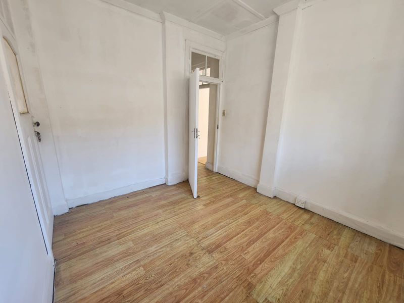 An empty bedroom featuring laminate flooring, white walls, and a classic door with a transom window above.