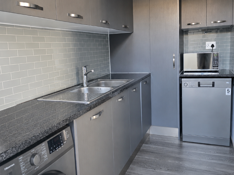 Modern scullery featuring sleek grey cabinetry, subway tile backsplash, laminate countertops, and integrated laundry and dishwashing appliances.