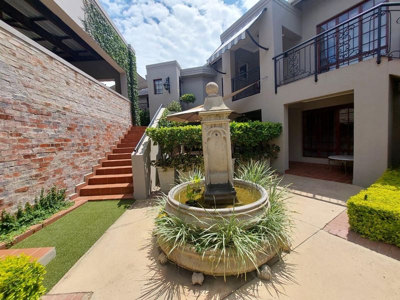 A well-maintained rear courtyard featuring a central stone fountain, brick retaining wall, tiled staircase, and a balcony with wrought iron railings.