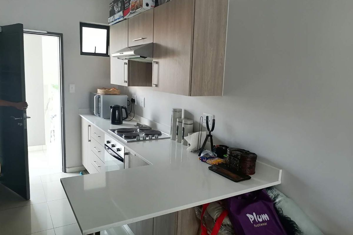 Modern kitchen featuring light wood cabinetry, white stone countertops, a built-in hob, oven, and extractor fan with tiled flooring.