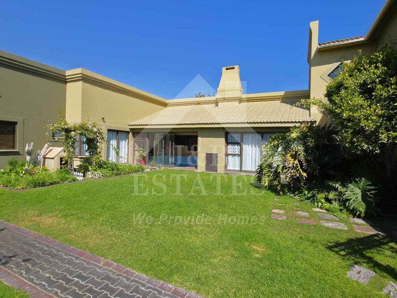 Rear view of the property featuring a well-maintained garden, paved walkway, and access to the home via sliding glass doors.