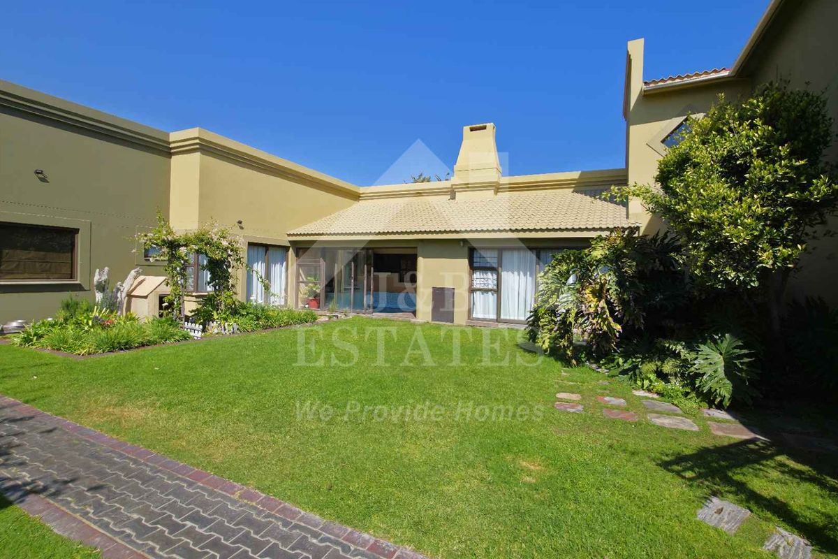 Rear view of the property featuring a well-maintained garden, paved walkway, and access to the home via sliding glass doors.
