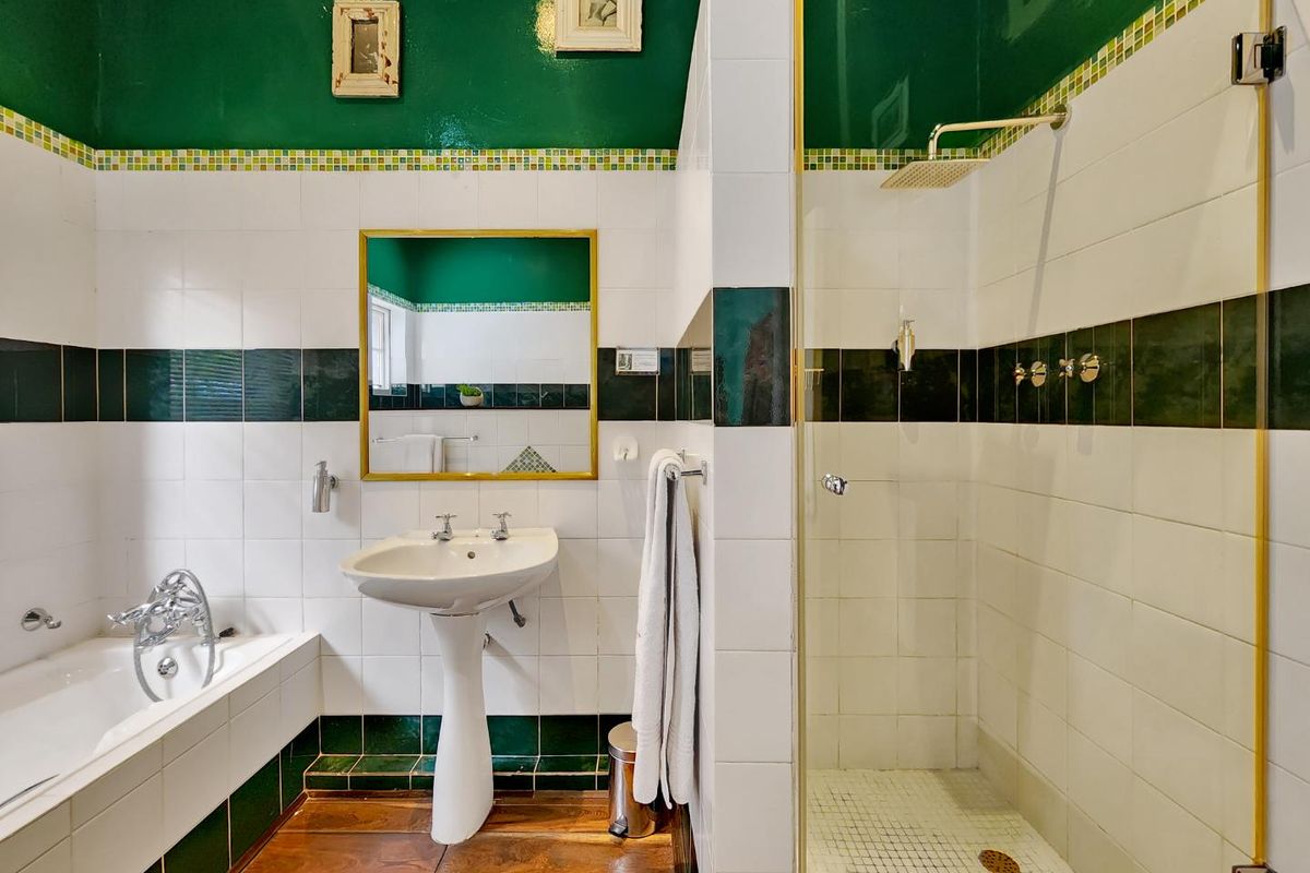 A bathroom featuring a pedestal basin, built-in bathtub, and a separate walk-in shower with green and white tiled finishes.