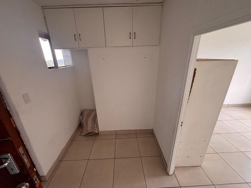 A small, empty utility or laundry area featuring tiled flooring and built-in overhead storage cabinets.