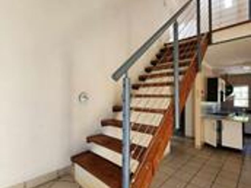 Open plan living area featuring a wooden staircase with metal balustrade and tiled flooring, leading to an upper level with a visible kitchen area.