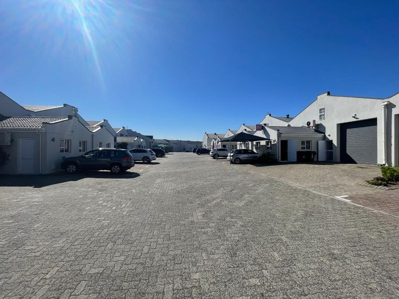 A view of a business park complex featuring paved driveways, multiple commercial units with roller shutter doors, and ample parking space.