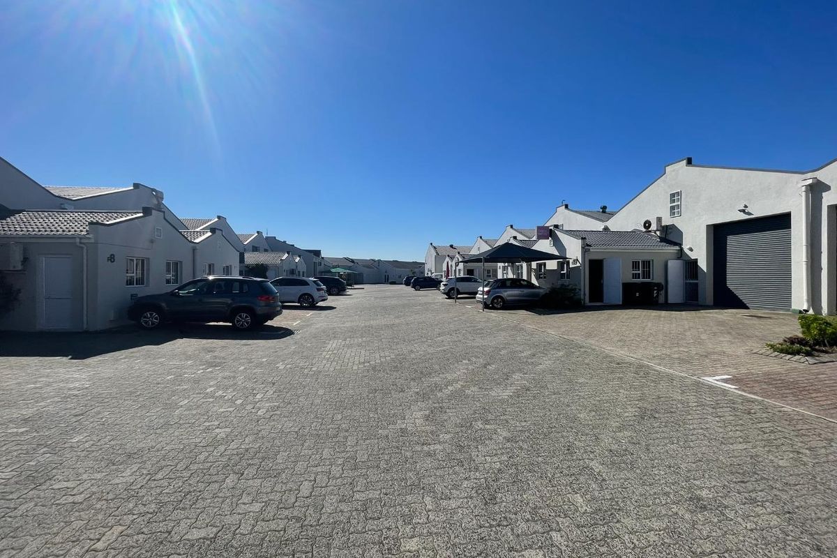 A view of a business park complex featuring paved driveways, multiple commercial units with roller shutter doors, and ample parking space.