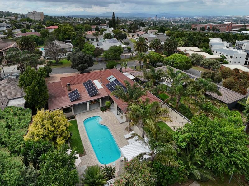 Aerial view of a residential property featuring a swimming pool, paved patio area, and solar panels installed on the tiled roof.