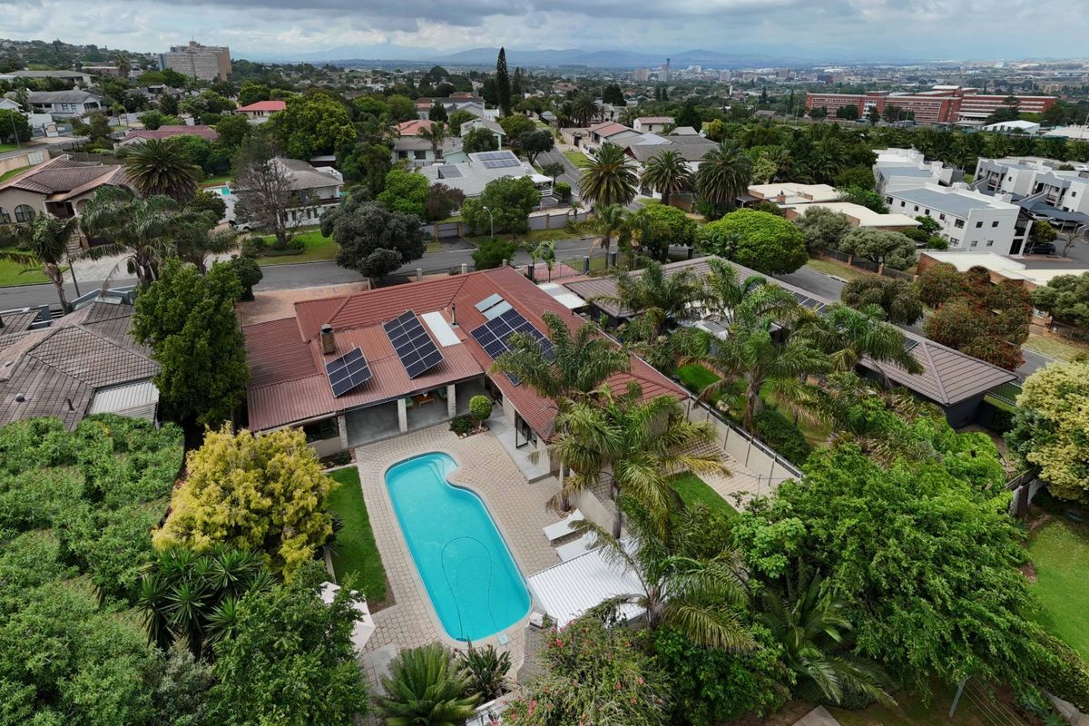 Aerial view of a residential property featuring a swimming pool, paved patio area, and solar panels installed on the tiled roof.