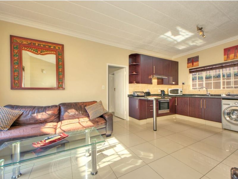 Open-plan living area featuring a kitchen with dark wood cabinetry, built-in oven, and tiled flooring, seamlessly connected to the lounge space.