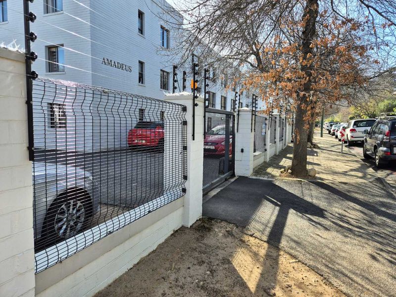 Front exterior view of the Amadeus apartment complex featuring secure perimeter walling, electric fencing, and gated vehicle access.