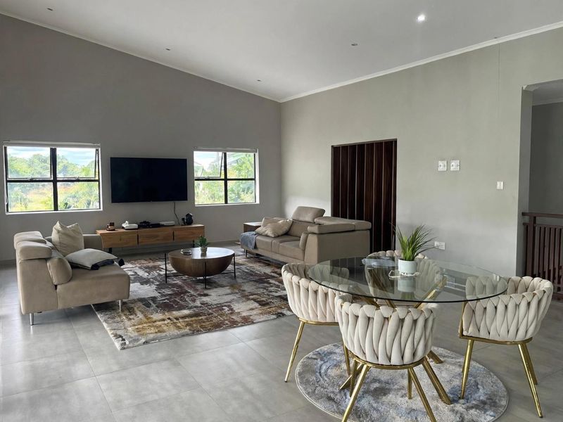 Spacious open-plan living and dining area featuring vaulted ceilings, large windows, and neutral tiled flooring, creating a bright and airy atmosphere.