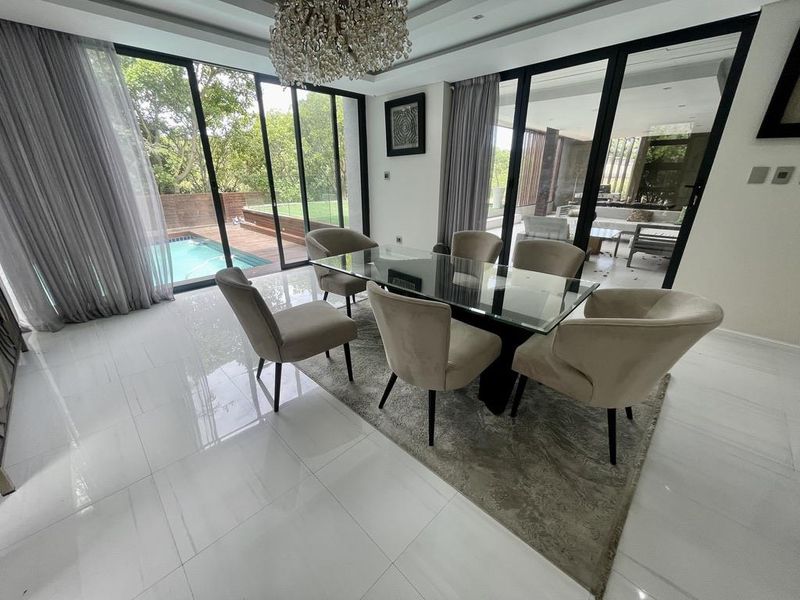 Elegant dining area featuring large format floor tiles, recessed ceiling lighting, and expansive floor-to-ceiling sliding glass doors providing views of the pool and garden.
