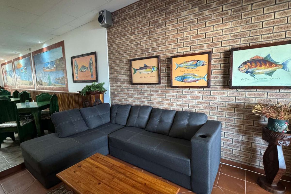 A spacious living area featuring a prominent exposed brick feature wall, tiled flooring, and integrated ceiling lighting.
