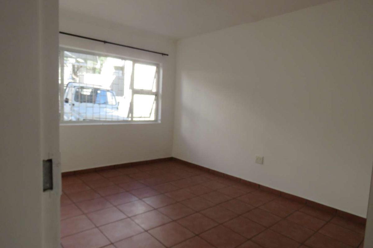 An empty bedroom featuring tiled flooring and a window fitted with security bars, offering a blank canvas for personalization.