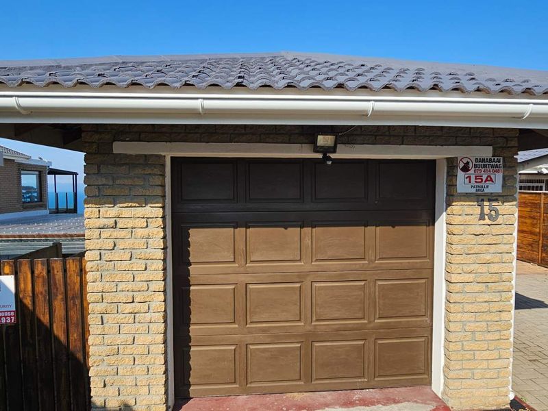 A detached single garage featuring a brown sectional door, brick construction, and a tiled roof, situated in a residential setting.