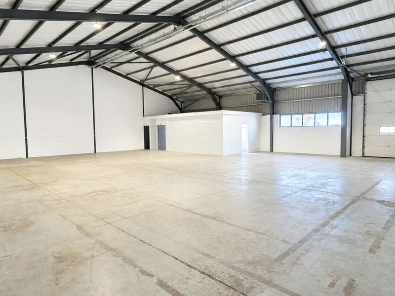 Spacious industrial warehouse unit featuring high ceilings with exposed steel portal frame, polished concrete flooring, and a large roller shutter door for easy access.