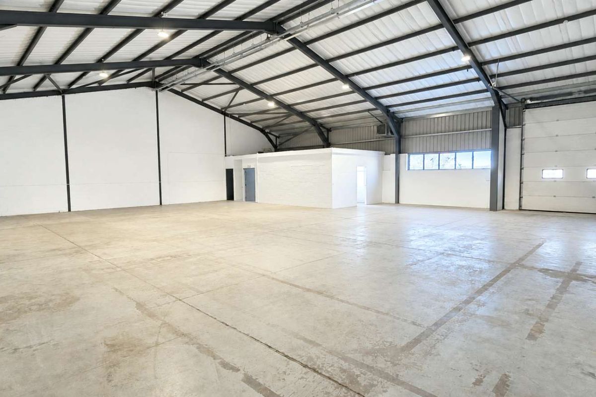 Spacious industrial warehouse unit featuring high ceilings with exposed steel portal frame, polished concrete flooring, and a large roller shutter door for easy access.