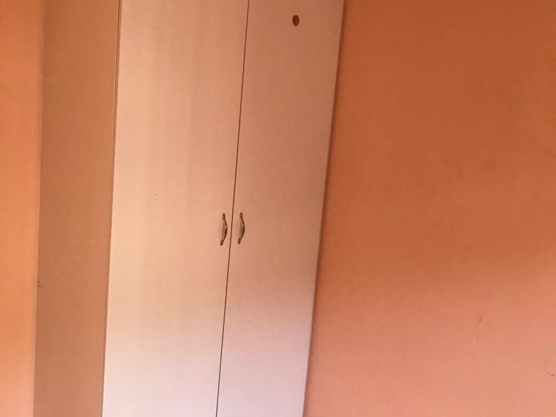 A bedroom featuring a built-in wardrobe, tiled flooring, and peach-colored walls with visible wear.