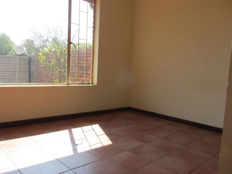 An empty bedroom featuring tiled flooring, neutral walls, and a window fitted with security bars, offering a blank canvas for personalization.