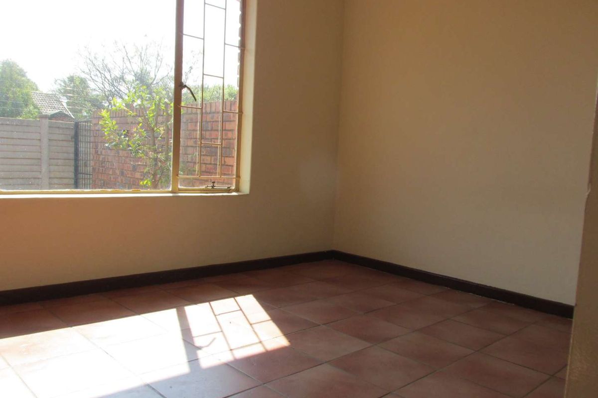 An empty bedroom featuring tiled flooring, neutral walls, and a window fitted with security bars, offering a blank canvas for personalization.