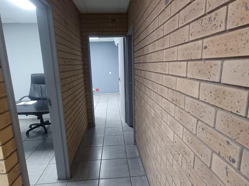 A functional office hallway featuring exposed brick walls, tiled flooring, and a drop ceiling with integrated air conditioning.