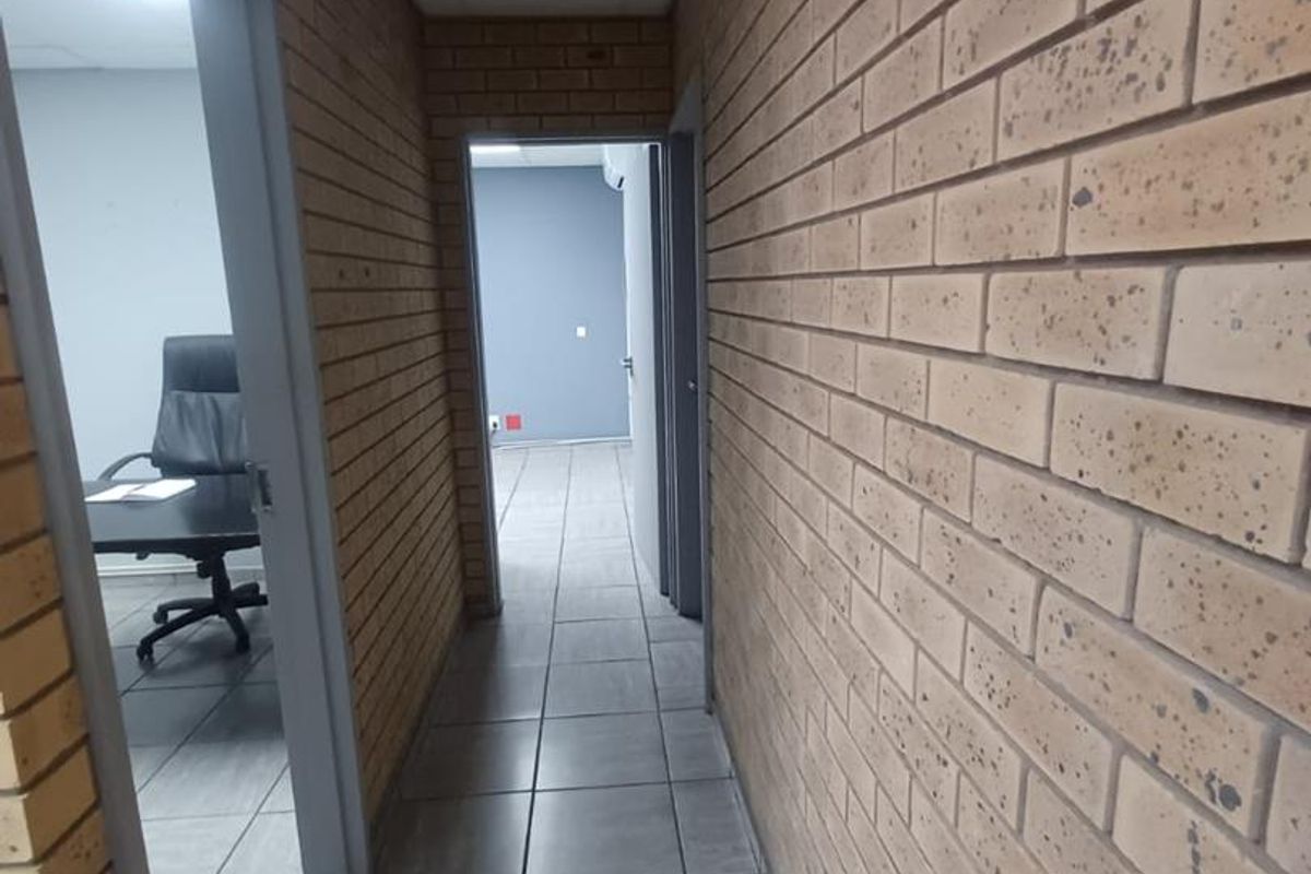 A functional office hallway featuring exposed brick walls, tiled flooring, and a drop ceiling with integrated air conditioning.