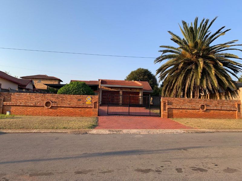 Front view of a residential property featuring a brick boundary wall, double garage, and a paved driveway with a secure metal gate.