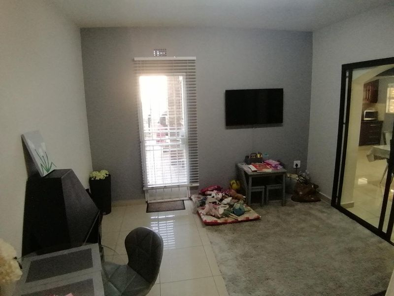 A living room featuring tiled flooring, a glass panel door with venetian blinds, and a wall-mounted television point, providing access to the exterior.