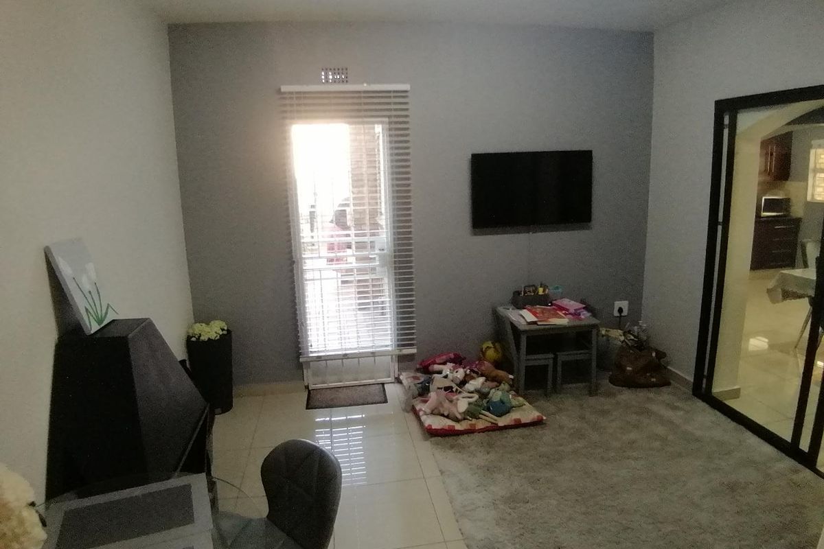 A living room featuring tiled flooring, a glass panel door with venetian blinds, and a wall-mounted television point, providing access to the exterior.