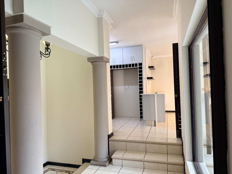 A bright, open-plan kitchen area featuring tiled flooring, built-in cabinetry, and a breakfast counter, accessible via a small set of stairs.