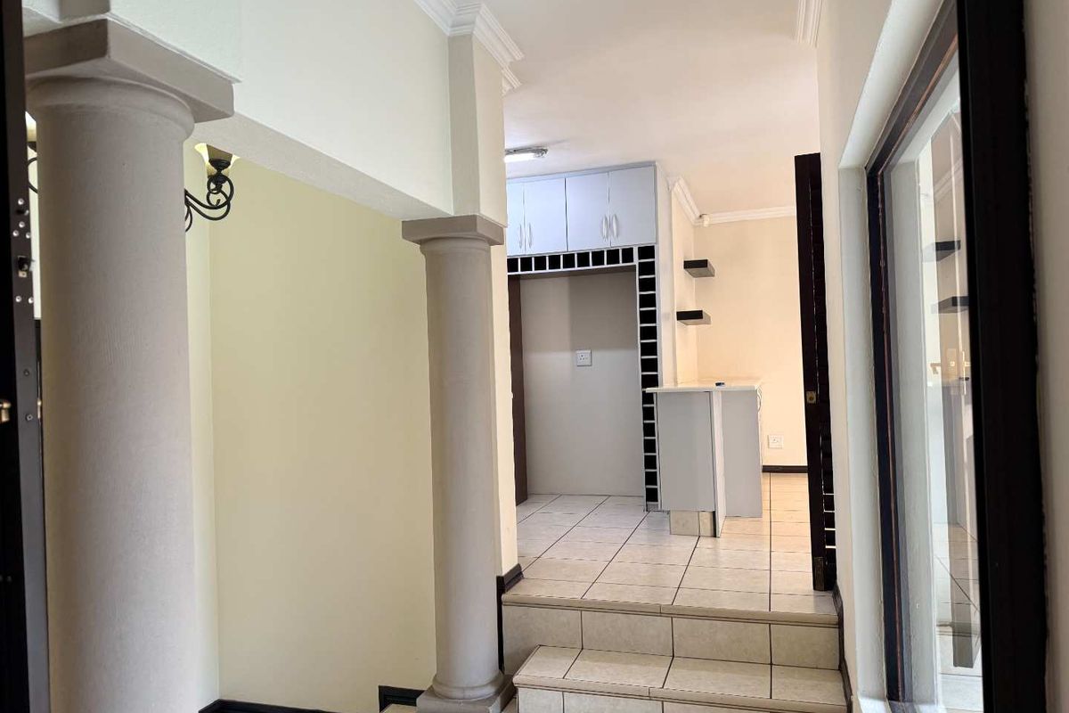 A bright, open-plan kitchen area featuring tiled flooring, built-in cabinetry, and a breakfast counter, accessible via a small set of stairs.