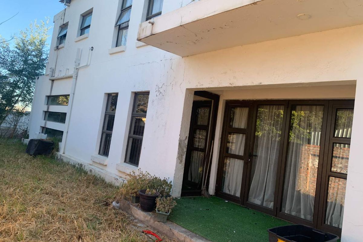 Rear elevation of the property featuring sliding glass doors, a concrete overhang, and visible wear to the exterior wall plaster and paint finish.