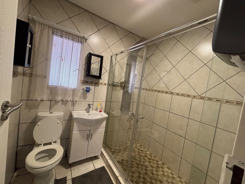 A functional bathroom featuring a glass shower enclosure, vanity basin, and toilet with neutral wall and floor tiling.
