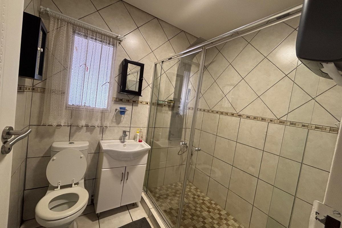 A functional bathroom featuring a glass shower enclosure, vanity basin, and toilet with neutral wall and floor tiling.