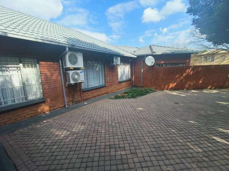 A front exterior view of a brick house featuring a paved driveway, tiled roof, and mounted air conditioning units.