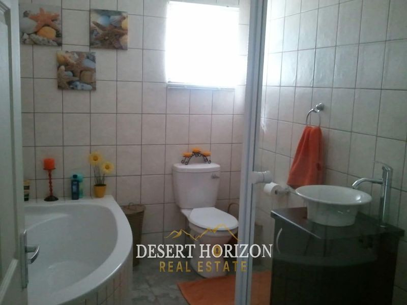 A functional bathroom featuring a bathtub, toilet, and a modern vessel sink set on a vanity cabinet with full-height wall tiling.