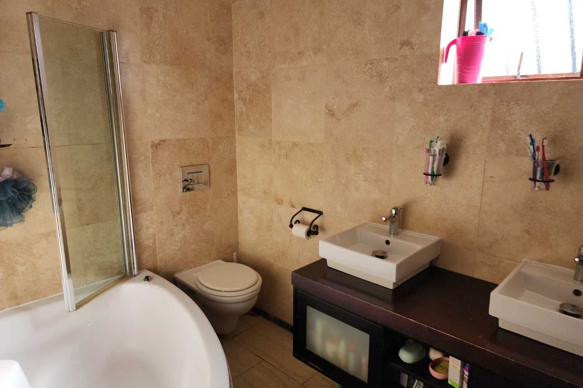 A functional bathroom featuring dual vessel sinks on a dark vanity, a bathtub with a glass screen, and floor-to-ceiling travertine-style wall tiling.