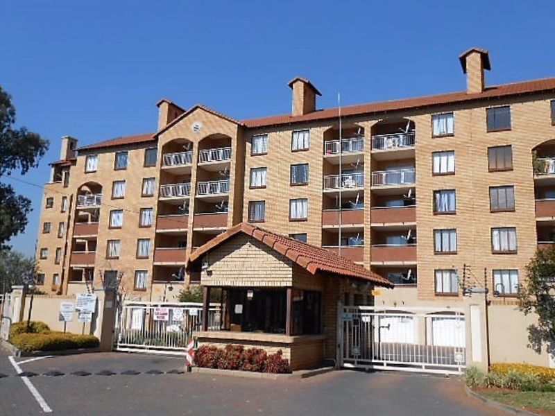 Front elevation of a multi-story apartment complex featuring a secure gated entrance, guard house, and private balconies for each unit.