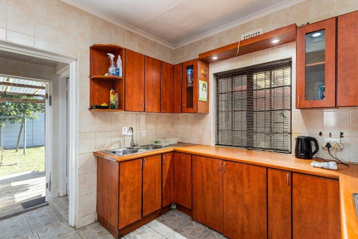 A functional kitchen featuring wood-look cabinetry, laminate countertops, a stainless steel sink, and tiled finishes with direct access to the outdoor area.
