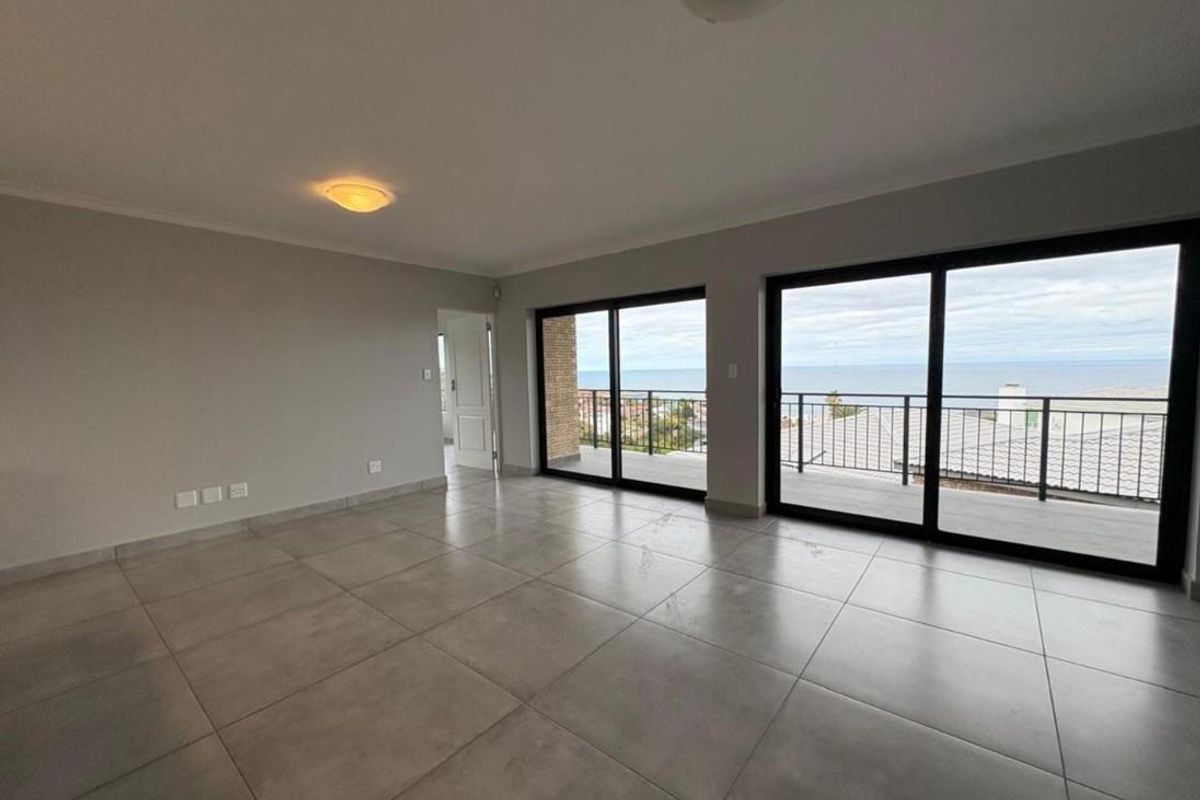 Spacious living area featuring large format floor tiles, neutral walls, and expansive sliding glass doors opening onto a balcony with ocean views.