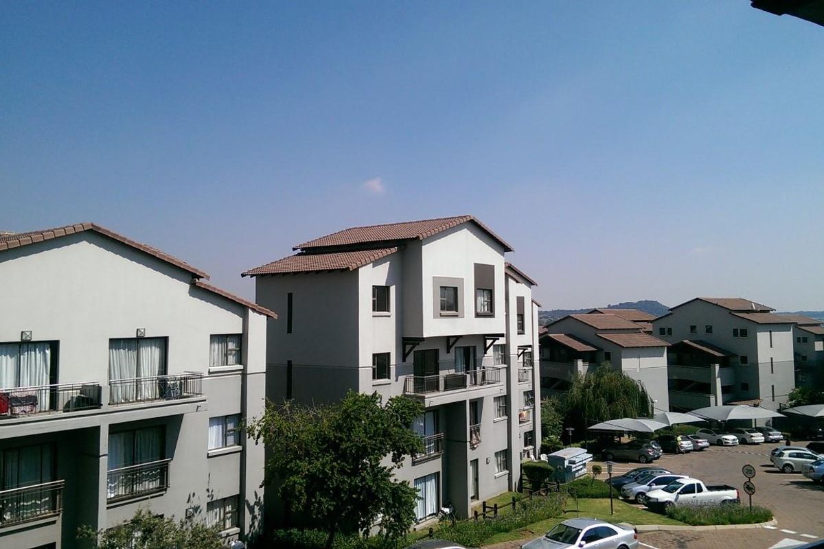 An elevated view of the apartment complex showing multiple residential buildings with tiled roofs, balconies, and a paved parking area with carports.