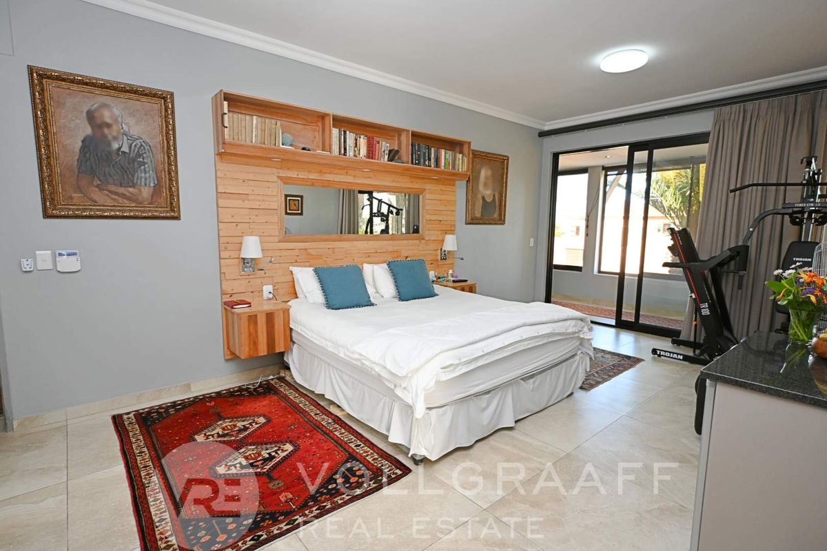 Spacious bedroom featuring built-in timber headboard with integrated shelving, tiled flooring, and sliding glass doors providing access to an outdoor area.