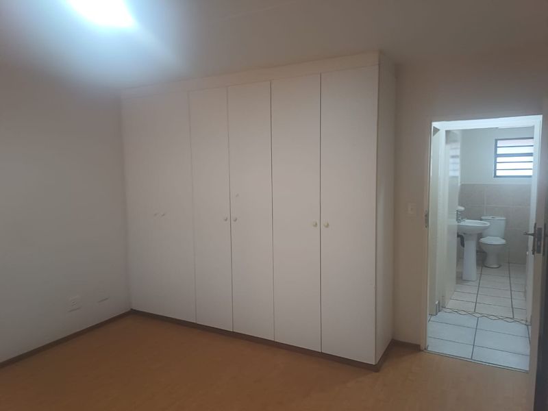A spacious bedroom featuring built-in cupboards, laminate flooring, and direct access to an en-suite bathroom.