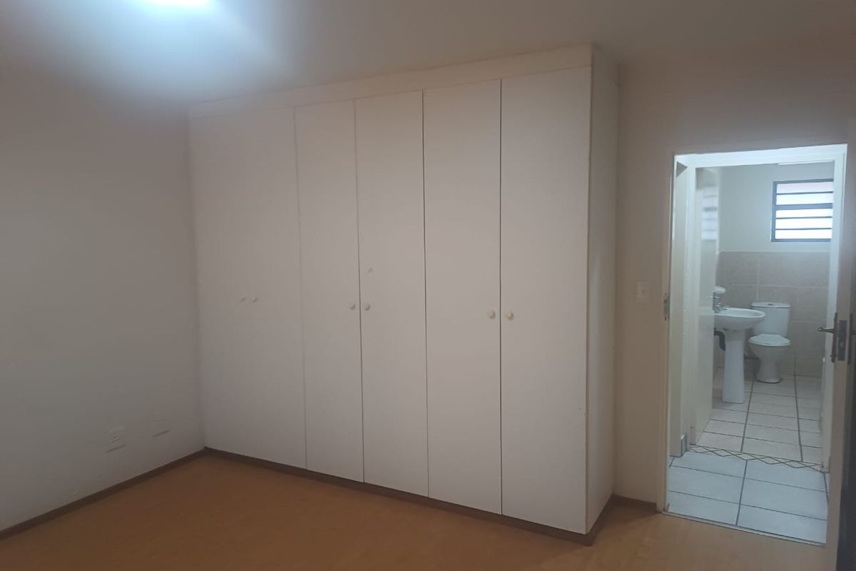 A spacious bedroom featuring built-in cupboards, laminate flooring, and direct access to an en-suite bathroom.