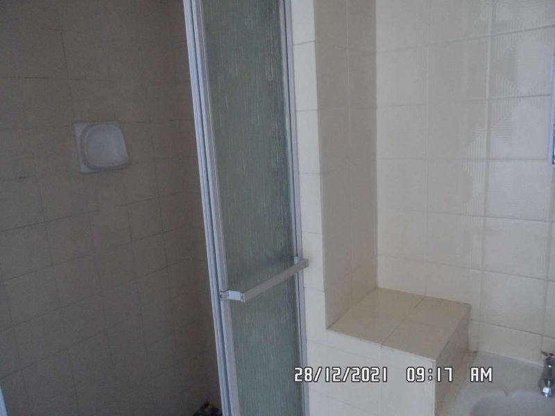 A dated bathroom shower area featuring tiled walls, a built-in tiled bench, and a glass shower enclosure.
