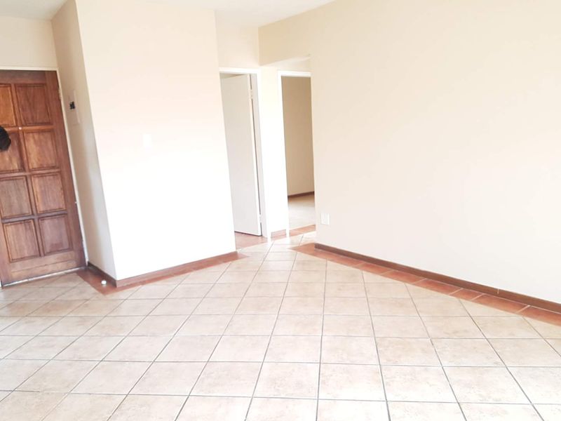 An empty living area featuring neutral walls, tiled flooring, and a wooden entrance door, providing a blank canvas for interior design.
