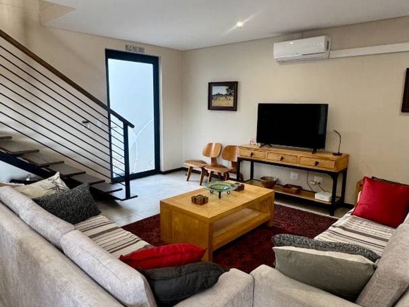 A well-lit living room featuring tiled flooring, a modern staircase with metal balustrades, and a wall-mounted split-system air conditioner.